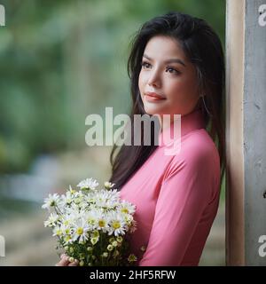 Ho Chi Minh City, Vietnam: Affascinante donna vietnamita in ao dai, scattando foto con crisantemi Foto Stock