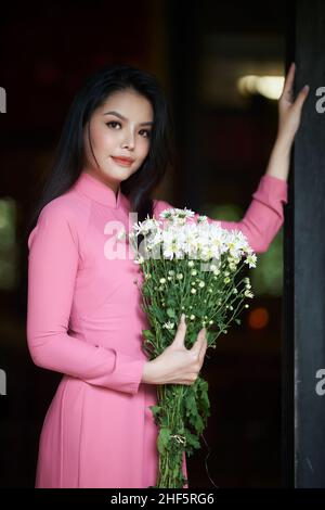 Ho Chi Minh City, Vietnam: Affascinante donna vietnamita in ao dai, scattando foto con crisantemi Foto Stock