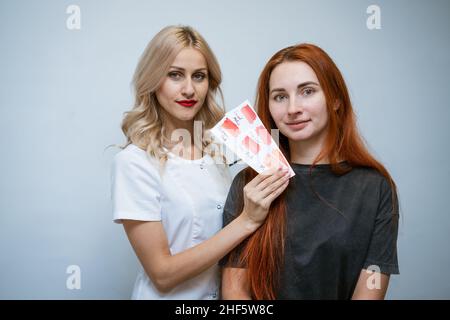 Sopracciglia e labbro sala tatuaggio, cosmetologo e permanente make-up master. Il master seleziona il colore desiderato del pigmento per le labbra e mostra le opzioni al cliente. Cosmetologia della bellezza Foto Stock