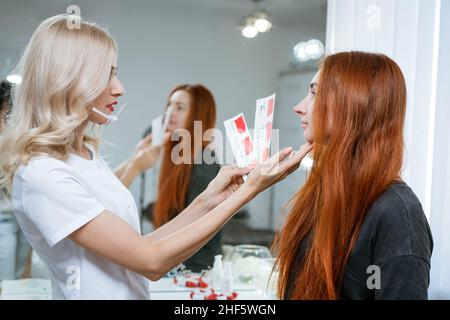 L'insegnante permanente di trucco dimostra il modello di esercitazione. Molto bello labbro e sopracciglia maestro nella sua officina. Ritratto di un makeup artista che sceglie il colore del trucco permanente sulle labbra Foto Stock