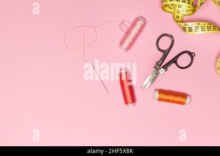 Spole colorate e accessori da cucire su sfondo rosa in una vista dall'alto Foto Stock