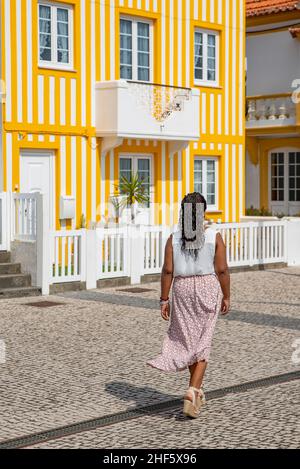 Bella giovane afroamericana sorridente mentre si cammina vicino a tipici edifici colorati sulla strada di Costa Nova, Aveiro, Portugal Lifestyle. Foto Stock