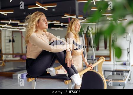 Focalizzata giovane donna che riposa dopo stretching e praticare alcune mosse ginniche in studio con il suo amico. Stile di vita sano, concetto sportivo Foto Stock