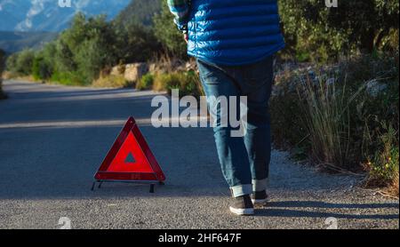 L'uomo con la schiena alla telecamera mette un triangolo segnaletico dietro la sua auto Foto Stock