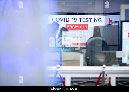 Le persone sono viste all'interno di una clinica di test Covid-19 il giorno di Boxing a Londra mentre gli acquirenti si riuniscono su Oxford Street nonostante le condizioni del tempo umido. Foto Stock