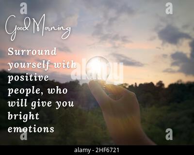 Citazioni motivazionali e ispiratrici - circondatevi di persone positive, che vi daranno emozioni luminose. Con una mano che tiene una lampadina e. Foto Stock