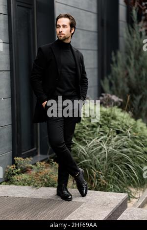 Uomo d'affari serio e sicuro in abito elegante fuori dall'ufficio, guardando lateralmente. Bel maschio di successo in stoffa di moda che funziona come Foto Stock