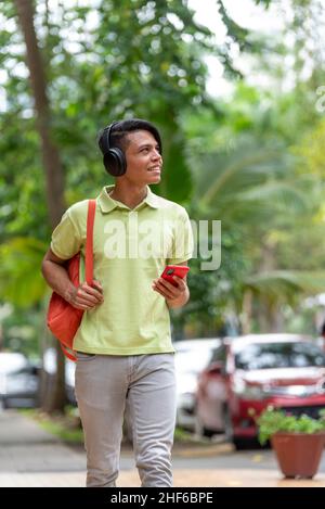 Giovane latino che cammina per la strada con il telefono in mano Foto Stock