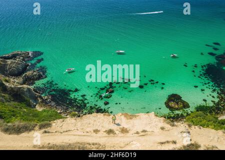 Uomo viaggiatore sul bordo di fronte alla spiaggia di Bounty con mare azzurro cristallino in una giornata di sole. Capo Fiolent a Sevastopol. Vista aerea. Foto Stock