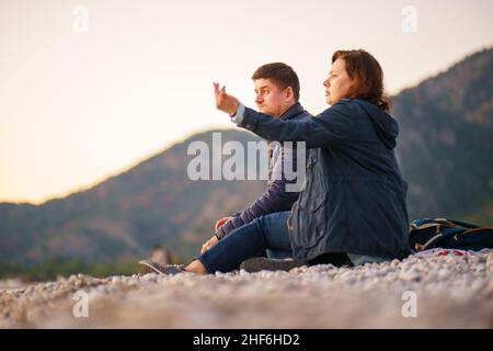 Viaggiatori. Marito e moglie. Data. Romanticismo. Una giornata nella natura. Un uomo e una donna si siedono su una spiaggia di pietra e godersi il mare d'inverno e un bel sole Foto Stock