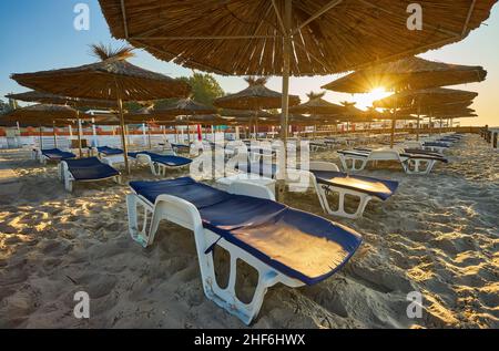 Dawn sulla spiaggia. Lettini e ombrelloni ai raggi del sole nascente. Spiaggia senza persone. Foto Stock