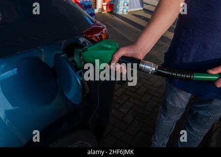 Uomo che tiene la pompa a benzina che riempie l'auto blu in una stazione di benzina con carburante quale benzina o diesel. Aumento dei prezzi del gas e del carburante concetto Foto Stock