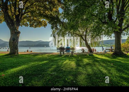 Coppia anziana felice seduta in estate vicino al lago durante il tramonto. Foto Stock