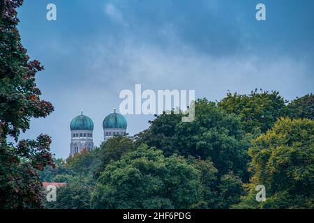 Ammira le cime delle due famose torri della Frauenkirche di Monaco, baviera, su cime degli alberi verdi e autunnali Foto Stock