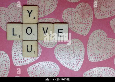 Concetto di amore e romanticismo. L'amore scrisse su scrabble giocando a cubetti su un cuore rosa sfondo. Giorno di San Valentino, concetto romantico, compagnia e ven Foto Stock