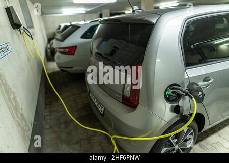 Collegato in filo di carica a un'auto elettrica in un garage di carico domestico con altre auto. Scena autentica del nuovo processo di rifornimento dell'auto a casa invece di andare alla stazione di servizio successiva Foto Stock