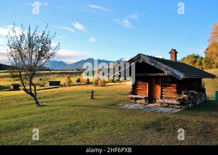 Capanna nei prati umpback vicino a Mittenwald, alberi, cielo bianco-blu, montagne sullo sfondo, armonioso Foto Stock