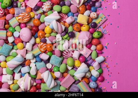 Draghe, caramelle, lecca lecca, marshmallows, dolci e brillanti per feste di divertimento su sfondo rosa Foto Stock