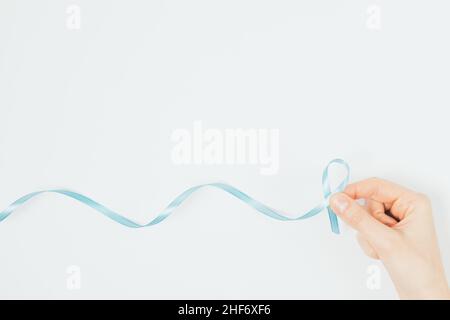 Mano della donna che tiene il nastro blu simbolo della Giornata Mondiale del cancro su sfondo bianco con spazio di copia Foto Stock