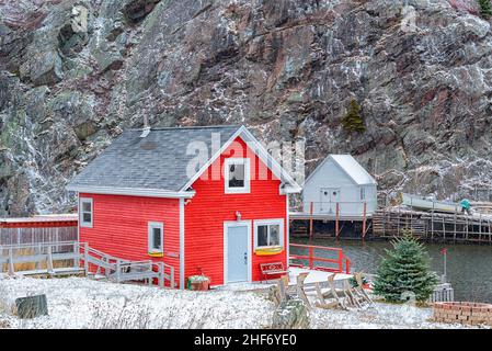 Edifici storici di stoccaggio della pesca rossa a St. John's, Terranova con una leggera spolverata di neve sulla scogliera rocciosa e gli alberi con l'oceano dietro. Foto Stock