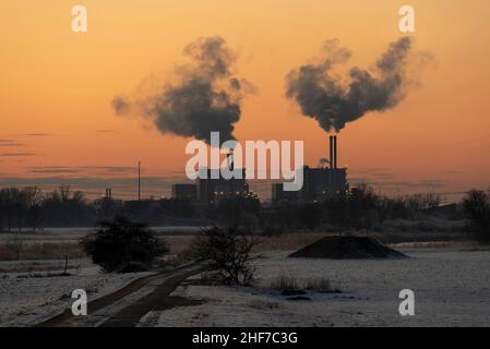 I camini dell'impianto di incenerimento dei rifiuti di Magdeburg fumano mentre il sole tramontato scolorisce il cielo. Foto Stock