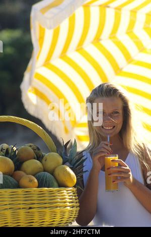 giovane bella bionda capelli donna ritratto bere succo d'arancia giallo ombrello dietro il viso sorridente sudore e giallo umbrellabackground evocazione estiva Foto Stock