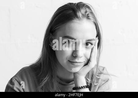 Giovane sorridente ragazza, primo piano ritratto in bianco e nero studio con luce naturale su parete bianca Foto Stock