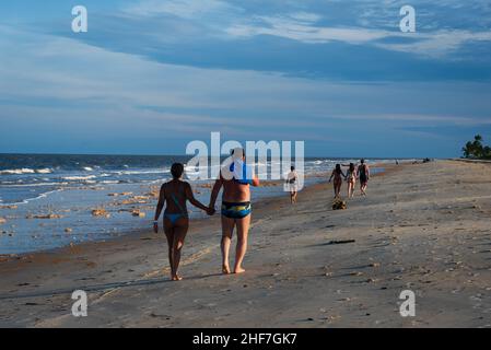 Vista posteriore dei bagnanti che camminano sulla sabbia tenendo le mani a Guaratiba Beach, Prado, Bahia, Brasile durante il tramonto. Foto Stock