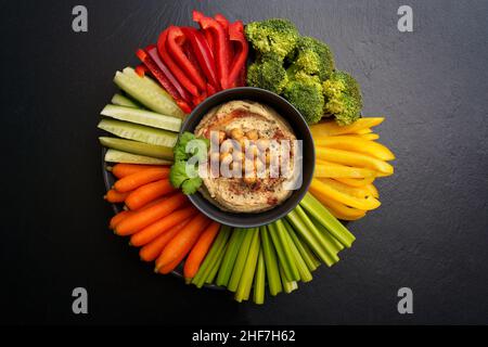 Vista dall'alto del gustoso hummus di ceci in piatto nero con verdure fresche su sfondo nero Foto Stock