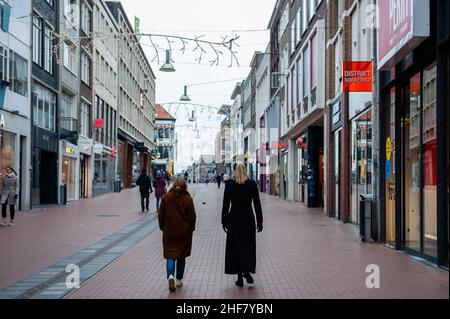 Due donne sono viste camminare nel mezzo di una delle strade dello shopping con negozi chiusi.Tonight, il gabinetto è previsto per annunciare un rilassamento delle regole del coronavirus per l'istruzione superiore, al dettaglio, le professioni di contatto e lo sport. Nel frattempo, le industrie culturali e della ristorazione dovranno attendere un po' più a lungo. L'Aia afferma che il gabinetto ha raggiunto un accordo in materia. I negozi possono rimanere aperti fino alle 5. Il numero massimo di visitatori per metro quadrato è ancora limitato. Il blocco duro è impostato per terminare il Sabato, 15 gennaio, e a causa dei consigli di Foto Stock