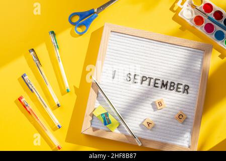 1 settembre lettera bordo con forniture scolastiche come penne, forbici, ABC, vernici su sfondo giallo. Istruzione. Giornata di conoscenza, studio, ritorno a scuola con Foto Stock