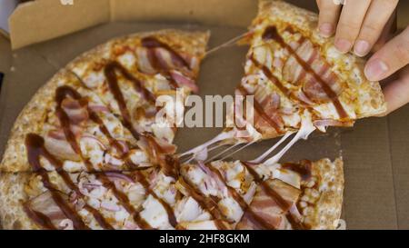 Donna mano prende una fetta di pizza con pollo e salsa barbecue. Vista dall'alto della pizza italiana adagiata su una scatola di cartone, concetto di cibo. Foto Stock