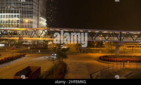 Passerella con passersby sopra la strada sullo sfondo notturno della città. Ponte pedonale con persone che camminano sulla notte edifici della città sfondo. Foto Stock