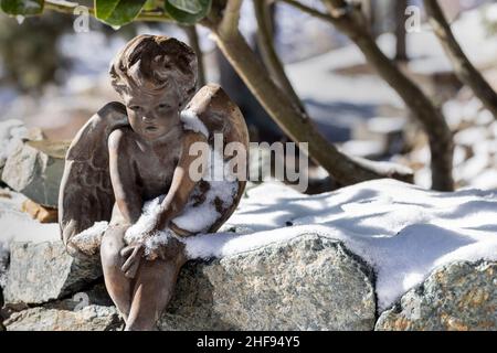 Parete di roccia con neve e un cherubino seduto con le ali aperte Foto Stock