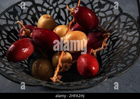 Rosso e giallo crudo datteri frutta o Kurma Muda (Ruthob) sul cesto vintage sopra il rustico sfondo. Foto Stock