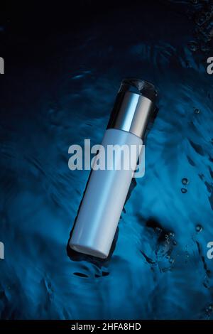 Mascherina cosmetica bianca in fondo blu fantasia acqua con bolla pop flusso in acqua , per pubblicità cosmetica , vista frontale , cosmetici fotografici Foto Stock