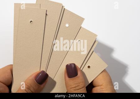 Mazzo di cartoncini rettangolari vuoti con piccoli fori nella parte superiore delle mani femminili con ombre che cadono su sfondo bianco. Tag mock up. Copia Foto Stock