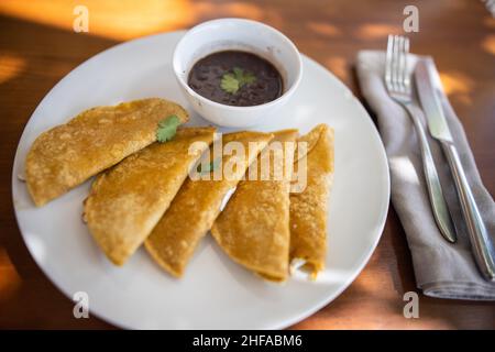 Piatto con quesadilla tradizionale e tazza di fagioli su tavola marrone Foto Stock