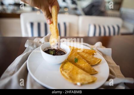 Immergere manualmente la quesadilla in una tazza di fagioli sopra il piatto bianco Foto Stock