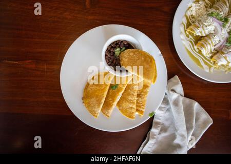 Deliziosi tacos con cestino tradizionale e una tazza di fagioli sopra il tavolo marrone Foto Stock