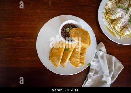 Deliziosi tacos con cestino tradizionale e una tazza di fagioli sopra il tavolo marrone Foto Stock