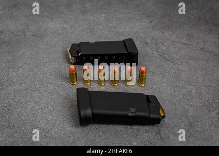 45 pallottole a punta cava di calibro ACP e a camicia completamente in metallo caricate in riviste di pistole a mano e rotonde non sparate allineate su una superficie di pietra Foto Stock