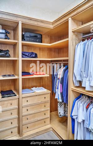 Elegante passeggiata in armadio con mobili in legno massello di acero e impiallacciatura per lo stoccaggio di vestiti con corona di stampaggio in appartamento Foto Stock