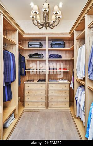 Elegante passeggiata in armadio con mobili in legno massello di acero e impiallacciatura per lo stoccaggio di vestiti con corona di stampaggio in appartamento Foto Stock