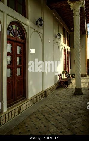 Lungo balcone sospeso all'ultimo piano dell'hotel per l'accesso alle camere con porte in legno, doppie, ovali, finestre e supporti di colonne intrecciate Foto Stock