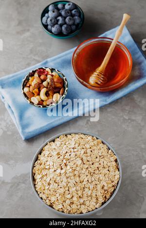 Sana farina d'avena da colazione con frutti di bosco, noci e miele. Fiocchi di avena, mirtilli, miele e noci assortite su sfondo grigio. Colazione vegana con oa Foto Stock