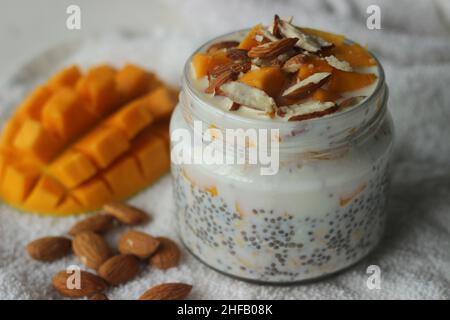 Oats durante la notte con mango e mandorle. Prodotto immergendo l'avena arrotolata e i semi di chia nel latte servito con manga tritati, mandorle e miele per un freddo Foto Stock