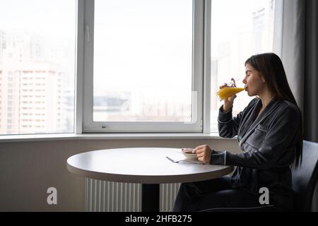 Giovane donna che gode di succo d'arancia fresco. Nella sua cucina, la signora sta bevendo il suo frullato appena fatto pieno di vitamine. Stile di vita sano . Banner. Foto Stock