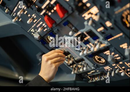 Primo piano della mano di un pilota che gira un interruttore a levetta sul pannello di controllo. Foto Stock