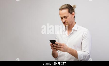 Giovane bionda bearded uomo che texting messaggio su smartphone su uno sfondo bianco studio con spazio copia Foto Stock
